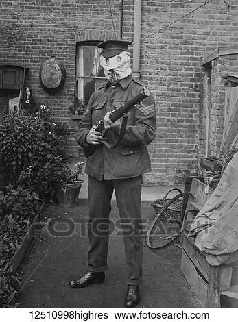 Stock Photograph - Magic lantern slide WW1, 1914-1918, World war one images. A British soldier ( seargent ) in a gas mask with rifle in house back yard..usual houshold things in the yard/garden, bicycle wheel, batth tub and basket.. Fotosearch