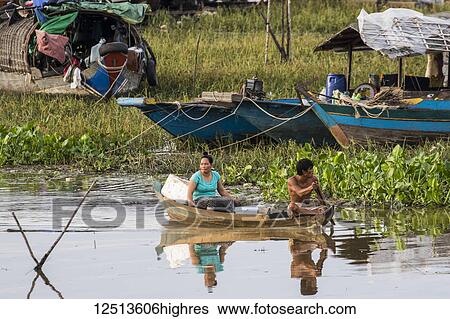 Stock Photograph - Man and woman in a boat by a floating village in the Tonle Sap; Siem Reap, Cambodia. Fotosearch