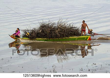 Stock Photograph - Man and woman with a child on a boat laden with wood approaching a floating village in the Tonle Sap; Siem Reap, Cambodia. Fotosearch