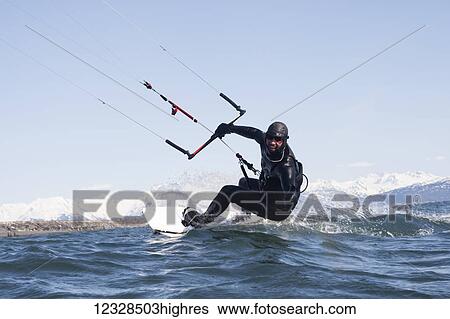 Stock Photograph - Man kitesurfing with Kenai Mountains in the background, Homer, South-central Alaska; Homer, Alaska, United States of America. Fotosearch