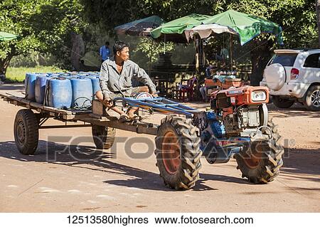 Stock Photograph - Man riding a tractor down the street, Beng Meala; Siem Reap, Cambodia. Fotosearch