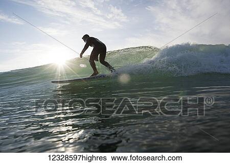 Stock Photograph - Man surfing and backlit by the sunlight, South-central Alaska; Homer, Alaska, United States of America. Fotosearch