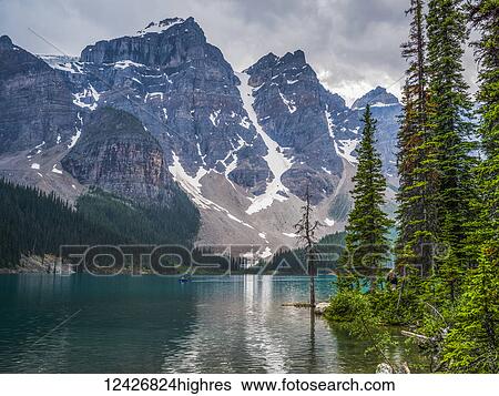Stock Photograph - Moraine Lake and the rugged peaks of the Canadian Rocky Mountains with a boat in the water; Lake Louise, Alberta, Canada. Fotosearch