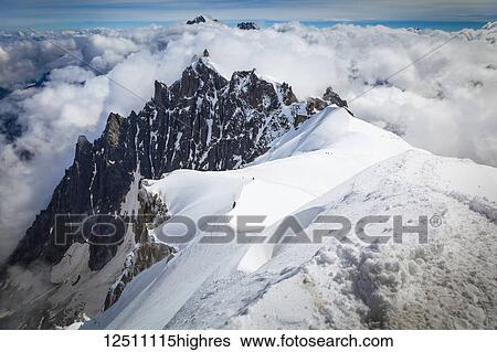 Stock Photograph - Mountain climbers departing Aiguille du midi, Aiguille du Plan summit in the background; Chamonix-Mont-Blanc, Haute-Savoie, France. Fotosearch