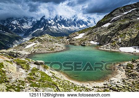 Stock Photograph - None Lac Blanc, looking towards Mont Blanc Massif and Mer de Glace under dramatic clouds; Chamonix-Mont-Blanc, Haute-Savoie, France. Fotosearch