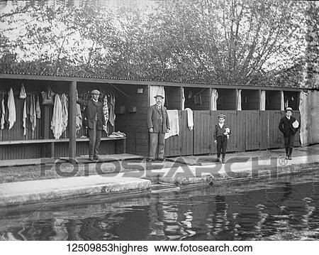 Stock Photograph - Outdoor swimming pool in the Victorian era with two boys waiting to go for a swim, circa 1900. Magic lantern slide.. Fotosearch