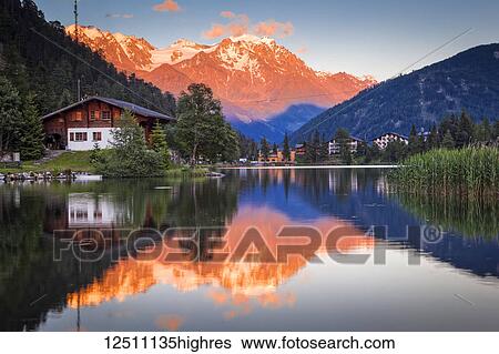 Stock Photograph - Pastel-coloured sunset glow on the mountains reflecting on Champex Lake; Champex, Valais, Switzerland. Fotosearch