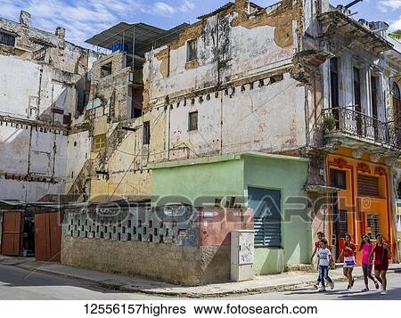 Stock Photograph - Pedestrians walk on the street past a run-down building; Havana, Cuba. Fotosearch