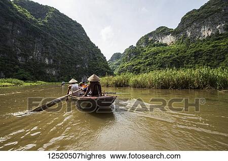 Stock Photograph - People in a boat on the Ngo Dong River surrounded by limestone karst mountains; Tam Coc, Ninh Binh, Vietnam. Fotosearch