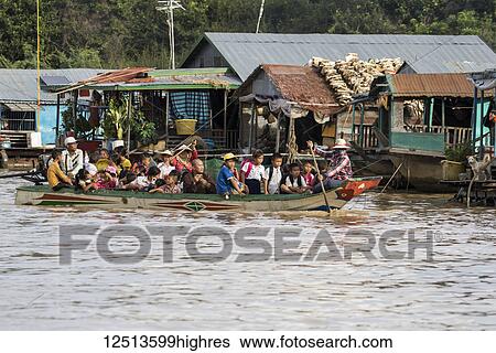 Stock Photograph - People in a public boat by a floating village in the Tonle Sap; Siem Reap, Cambodia. Fotosearch
