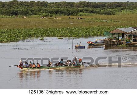Stock Photograph - People in a public boat by a floating village in the Tonle Sap; Siem Reap, Cambodia. Fotosearch