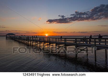 Stock Photograph - People standing on a pier as the sun sets over the Indian River; Indialantic, Florida, United States of America. Fotosearch