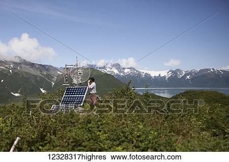 Stock Photograph - Person With Cell Phone Next To A Solar Panel With The Kenai Mountains In The Background, Kachemak Bay State Park, Southcentral Alaska, USA. Fotosearch