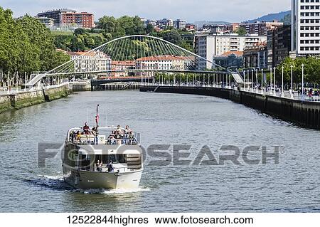 Stock Photograph - Pleasure boat cruising on the River Nervion with Zubizuri Bridge in the background; Bilbao, Vizcaya, Pais Vasco, Spain. Fotosearch