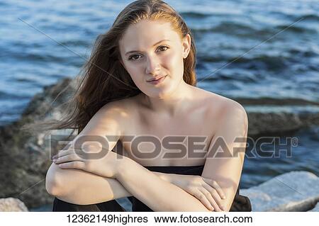 Stock Photograph - Portrait of a teenage girl sitting on rocks at Woodbine Beach in summer; Toronto, Ontario, Canada. Fotosearch