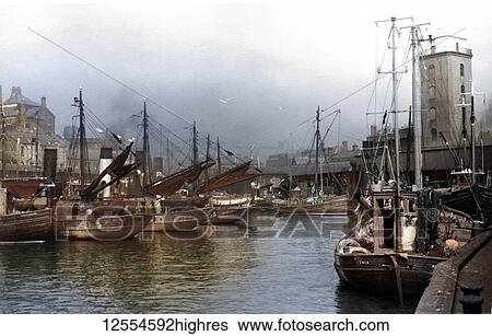 Stock Photograph - Postcard circa 1900, Victorian/Edwardian Social History. A view of North Shields Fish Quay with fishing boats and buildings. Low light (lighthouse) also in view; North Shields, Tyne and Wear, England. Fotosearch