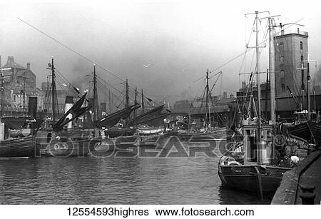 Stock Photograph - Postcard circa 1900, Victorian/Edwardian Social History. A view of North Shields Fish Quay with fishing boats and buildings. Low light (lighthouse) also in view; North Shields, Tyne and Wear, England. Fotosearch