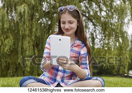 Preteen girl sitting in a park holding a tablet; Toronto, Ontario, Canada View Large Photo Image Stock Photograph - Preteen girl sitting in a park holding a tablet; Toronto, Ontario, Canada. Fotosearch