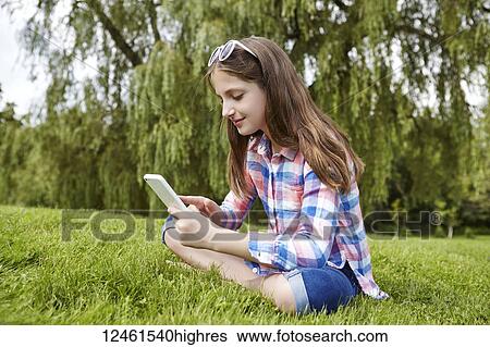 Preteen girl sitting in a park holding a tablet; Toronto, Ontario, Canada View Large Photo Image Stock Photograph - Preteen girl sitting in a park holding a tablet; Toronto, Ontario, Canada. Fotosearch