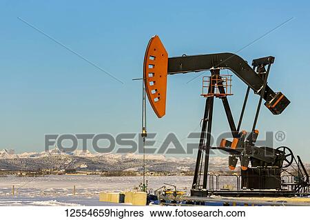 Pumpjack in a snow-covered field with snow-covered mountains and blue sky in the background, West of Airdrie; Alberta, Canada View Large Photo Image Stock Photograph - Pumpjack in a snow-covered field with snow-covered mountains and blue sky in the background, West of Airdrie; Alberta, Canada. Fotosearch