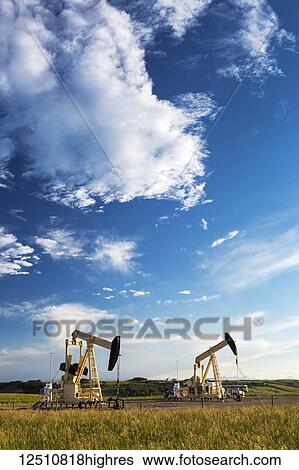 Stock Photograph - Pumpjacks with dramatic clouds and blue sky at sunset, West of Airdrie; Alberta, Canada. Fotosearch