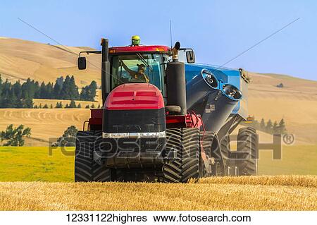 Stock Photograph - Quadtrac Tractor Pulling A Grain Cart In A Wheat Field During Harvest In The Palouse Region Of Eastern Washington; Washington, United States Of America. Fotosearch