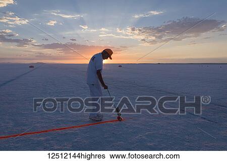 Stock Photograph - Race official sprays starting line at sunrise on Bonneville Salt Flats during Bonneville Speed Week 2017; Wendover, Utah, United States of America. Fotosearch