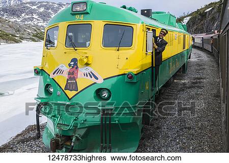 Stock Photograph - Railroad conductor rides the diesel White Pass Railroad engine on return to Skagway, Southeast Alaska; Skagway, Alaska, United States of America. Fotosearch