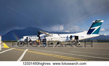 Stock Photograph - Rainbow Over The Terrace Kitimat Airport As Passengers Load A Plane On The Tarmac; Terrace, British Columbia, Canada. Fotosearch