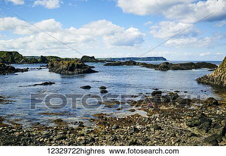 Stock Photograph - Rugged Coastline Of Northern Ireland With A Small Girl Sitting On The Rocks With A Net At The Water's Edge; Ireland. Fotosearch