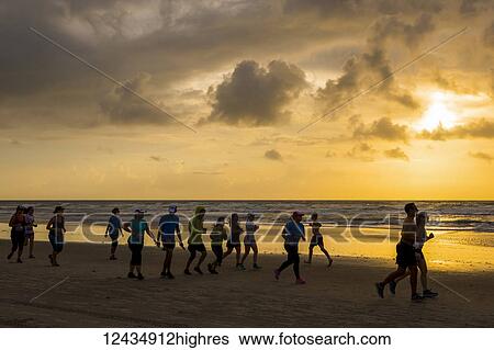Stock Photograph - Runners race on the beach at sunrise during the 2017 USA Beach Running Championships; Cocoa Beach, Florida, United States of America. Fotosearch