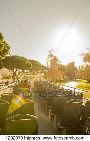 Stock Photograph - Seats In A Tour Bus With A View Of The Pedestrians, Palm Trees And Buildings In The French Riviera; Cannes, Cote D'azur, France. Fotosearch