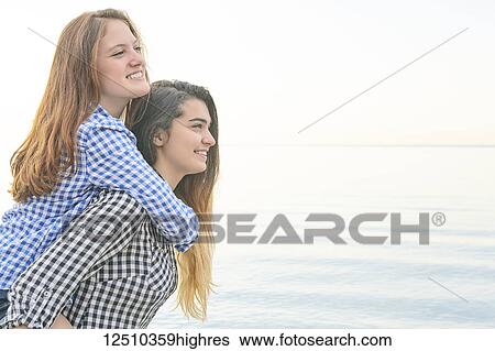 Side view of two teenage girls at the water's edge, one giving a ride to her friend on her back, Woodbine Beach; Toronto, Ontario, Canada View Large Photo Image Stock Photograph - Side view of two teenage girls at the water's edge, one giving a ride to her friend on her back, Woodbine Beach; Toronto, Ontario, Canada. Fotosearch