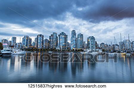 Stock Photograph - Skyline of residential buildings along the waterfront with boats in the harbour at dusk; Vancouver, British Columbia, Canada. Fotosearch