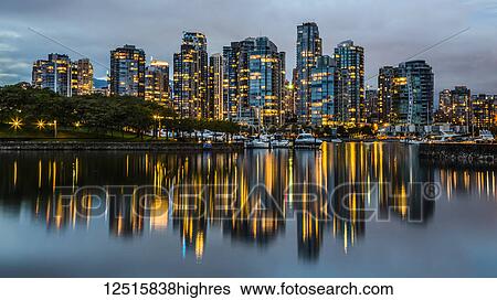 Stock Photograph - Skyline of residential buildings along the waterfront with boats in the harbour at dusk; Vancouver, British Columbia, Canada. Fotosearch
