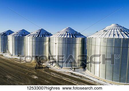 Stock Photograph - Snow-covered large metal grain storage bins with blue sky, South of Calgary; Alberta, Canada. Fotosearch