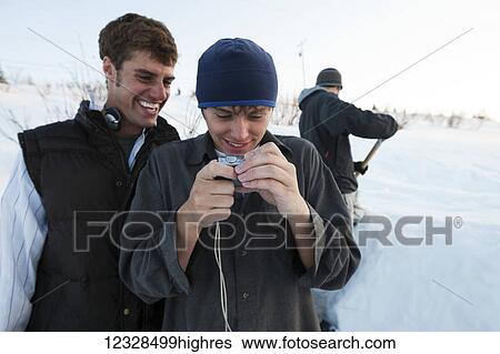 Stock Photograph - Snowboarders looking at pictures on a digital camera, South-central Alaska; Homer, Alaska, United States of America. Fotosearch