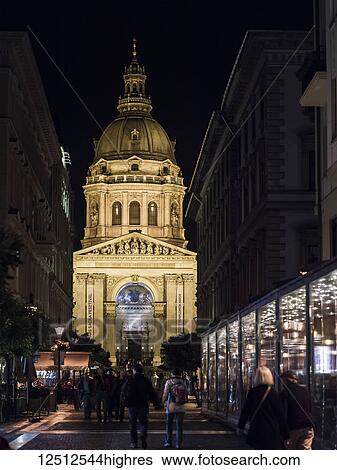 Stock Photograph - St. Stephen's Basilica illuminated at night with pedestrians on the street; Budapest, Budapest, Hungary. Fotosearch