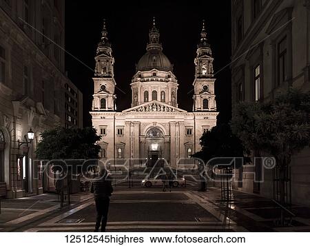 Stock Photograph - St. Stephen's Basilica illuminated at night with pedestrians on the street; Budapest, Budapest, Hungary. Fotosearch