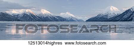Stock Photograph - Sunset lights up the snow-covered peaks of the Chugach Mountains along Turnagain Arm, sea ice covering reflections in the foreground, Turnagain Pass, Kenai Peninsula, South-central Alaska in winter; Alaska, United States of America. Fotosearch