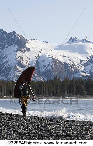 Stock Photograph - Surfer carrying his surfboard along the Kenai Peninsula Outer Coast, South-central Alaska; Alaska, United States of America. Fotosearch