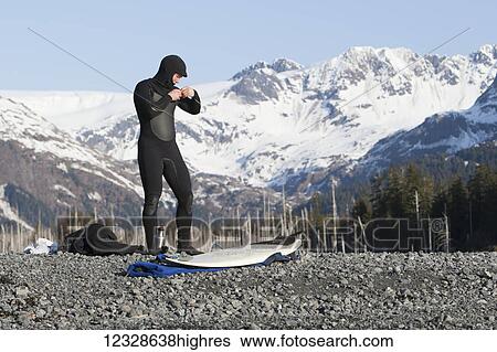 Stock Photograph - Surfer gearing up to go surfing on the Kenai Peninsula Outer Coast, South-central Alaska; Alaska, United States of America. Fotosearch