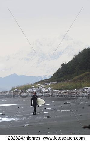 Stock Photograph - Surfer Holding Surfboard And Walking On Shore Near Yakutat, Southeast Alaska, USA. Fotosearch