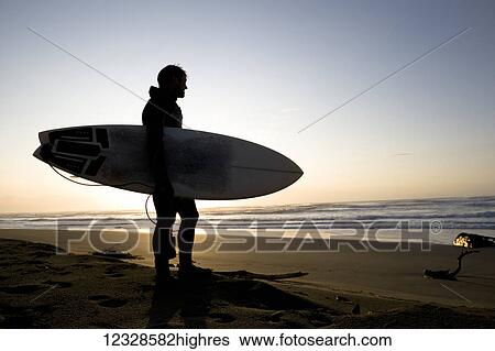 Surfer holding surfboard looking at ocean at sunset, Southeast Alaska; Yakutat, Alaska, United States of America View Large Photo Image Stock Photograph - Surfer holding surfboard looking at ocean at sunset, Southeast Alaska; Yakutat, Alaska, United States of America. Fotosearch
