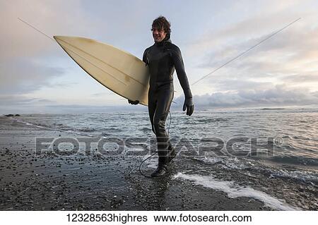 Stock Photograph - Surfer leaving the ocean, Southeast Alaska; Yakutat, Alaska, United States of America. Fotosearch