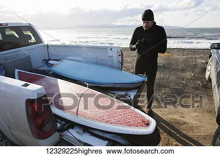 Stock Photograph - Surfer preparing gear next to a truck with surfboards, Southeast Alaska; Yakutat, Alaska, United States of America. Fotosearch