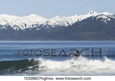 Stock Photograph - Surfer riding a wave on the Kenai Peninsula Outer Coast, South-central Alaska; Alaska, United States of America. Fotosearch