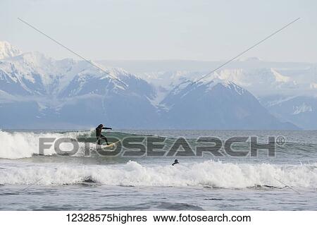 Surfer riding a wave with Fairweather Range in the background, Southeast Alaska; Yakutat, Alaska, United States of America View Large Photo Image Stock Photograph - Surfer riding a wave with Fairweather Range in the background, Southeast Alaska; Yakutat, Alaska, United States of America. Fotosearch