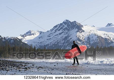 Stock Photograph - Surfer standing along the ocean on the Kenai Peninsula Outer Coast, South-central Alaska; Alaska, United States of America. Fotosearch