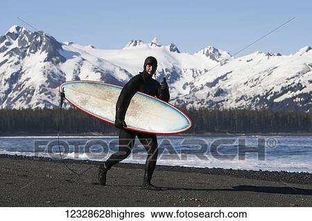 Stock Photograph - Surfer walking on the beach along the Kenai Peninsula Outer Coast, South-central Alaska, USA. Fotosearch